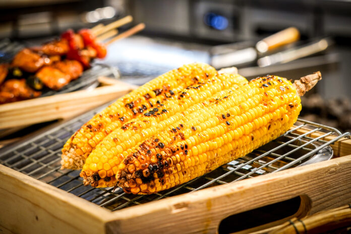 grilled corn on the grill with blur BBQ beside.