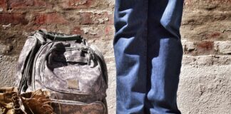 minimalist photography of person standing near backpack and boots