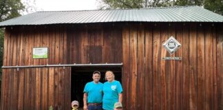 A man, a woman and two boys stand in front of a barn.