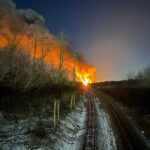 Two sides to every story A flame reaching high into the sky can be seen at the end of a railroad tracks that go up the middle of the photo.