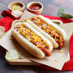 Chili dog, chili cheese hotdog served on wood tray with chips –