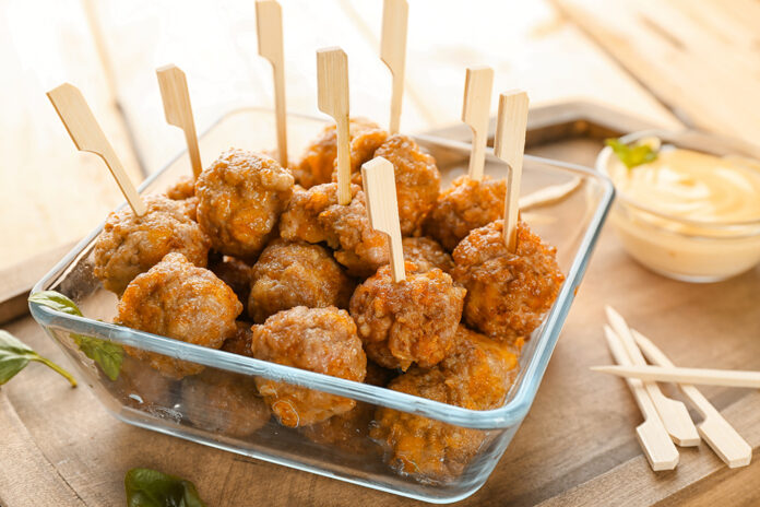 Glass dish with sausage cheese balls on wooden board